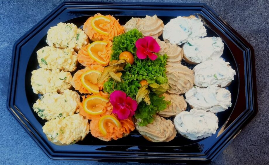 Tacki cateringowe z różnorodnymi przystawkami udekorowane kwiatami i owocami.